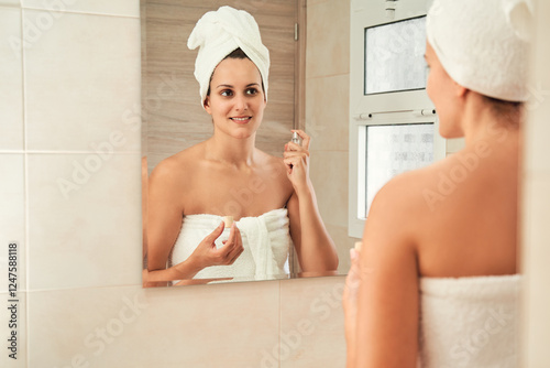Woman applying perfume in bathroom mirror reflection. Skincare concept.