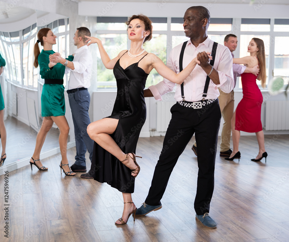 Fototapeta premium Woman with African man participants of dance workshop perform figure waltz. Students learn to dance classic salon dance, work out movements with partner in choreography studio.