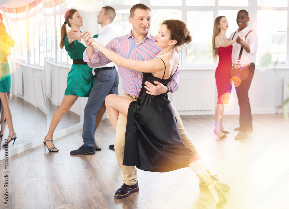 Fototapeta premium Positive middle-aged man and woman practicing waltz in pair in dancing studio