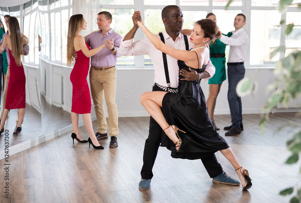 Fototapeta premium Pair of woman and African American man enjoying of sensual tango dance in choreo class. Exciting hobby, active lifestyle, passion for dancing and choreography