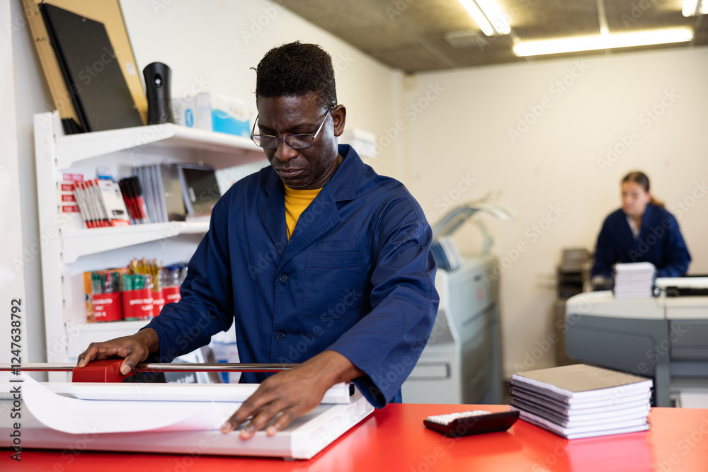 Serious print shop worker cuts paper on a professional cutter Serious print shop worker cuts paper on a professional cutter