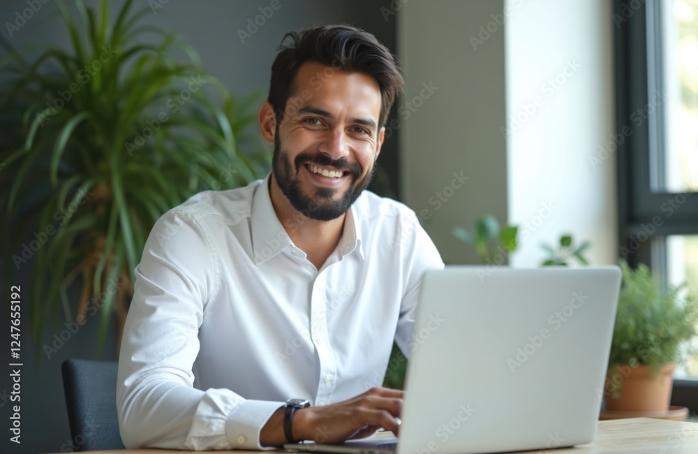 Happy businessman working on laptop in office. Smiling man using tech in modern indoor office environment. Pro looking at camera. Successful entrepreneur working remotely at wooden table. Interior Happy businessman working on laptop in office. Smiling man using tech in modern indoor office environment. Pro looking at camera. Successful entrepreneur working remotely at wooden table. Interior