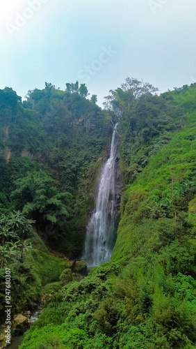 Aerial photo of the beautiful Surodipo Waterfall surrounded by high cliffs with lush trees all around. Aerial panorama of the waterfall located on the edge of a cliff among lush trees and steep cliffs