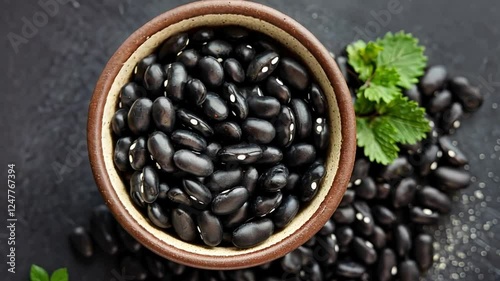 Top view of shiny black beans in a ceramic bowl on a dark background.
