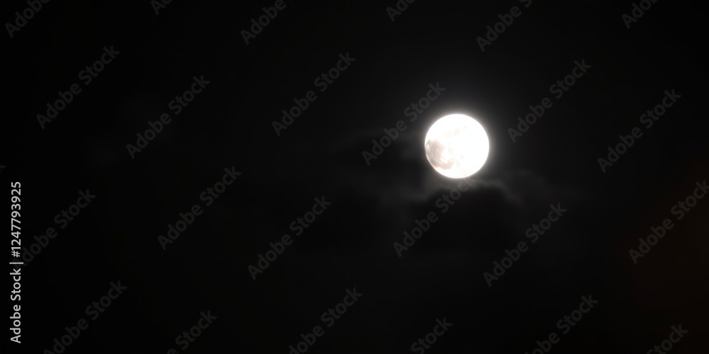 A full moon partially obscured by clouds in a dark night sky A full moon partially obscured by clouds in a dark night sky