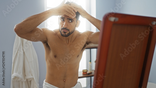 Young hispanic man with beard adjusting hair in mirror at spa showing focus and contemplation in wellness room with soft lighting creating serene indoor atmosphere. photo