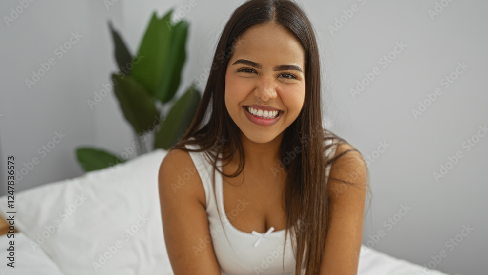 Woman smiling cheerfully, beautiful brunette sitting on bed in bright bedroom surrounded by houseplants, indoors setting highlighting attractive young adult person. Woman smiling cheerfully, beautiful brunette sitting on bed in bright bedroom surrounded by houseplants, indoors setting highlighting attractive young adult person.
