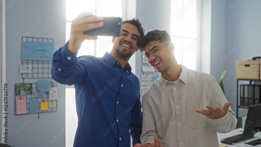 Fototapeta premium Hispanic men taking a selfie in an office, showcasing their work environment through a friendly and collaborative atmosphere.