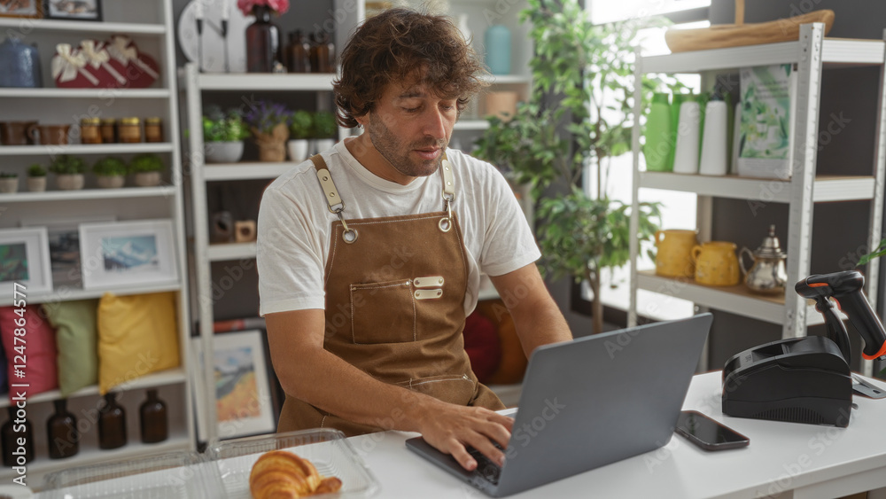 Fototapeta premium Young man working on laptop in home decor store with various decorations and plants in the background