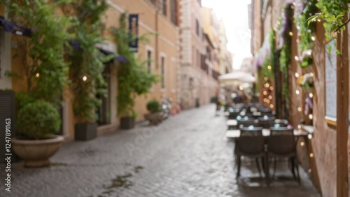 Blurred street scene in old town rome with bokeh effect showing charming italian outdoor cafe and cobblestone walkway lined with flowering plants and colorful buildings.