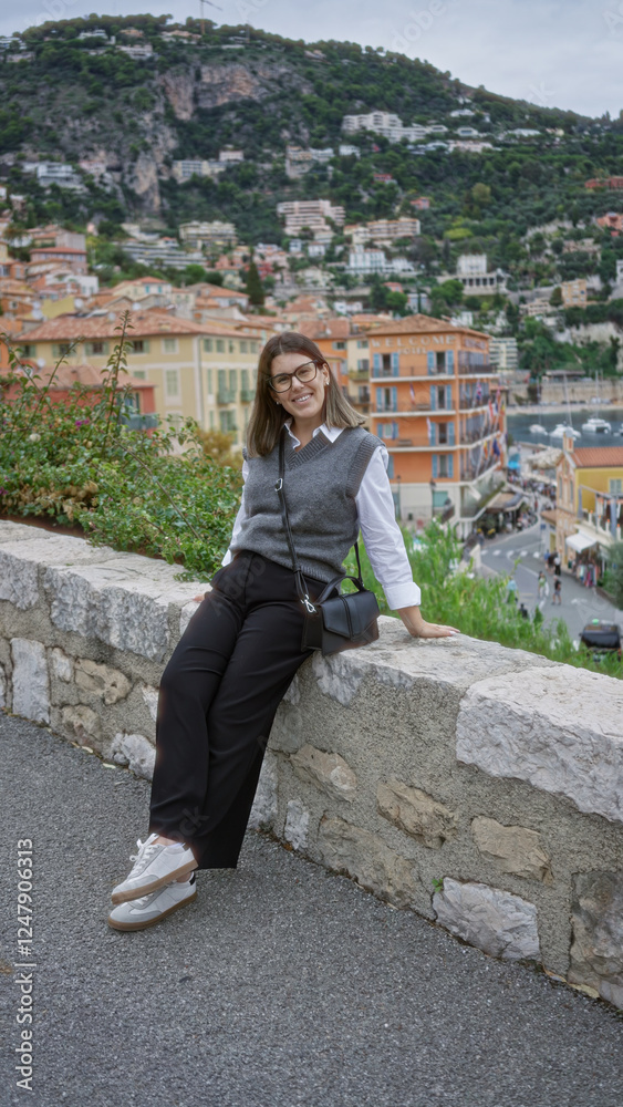 Fototapeta premium Woman smiling in villefranche france with picturesque mediterranean backdrop featuring colorful architecture and lush hills