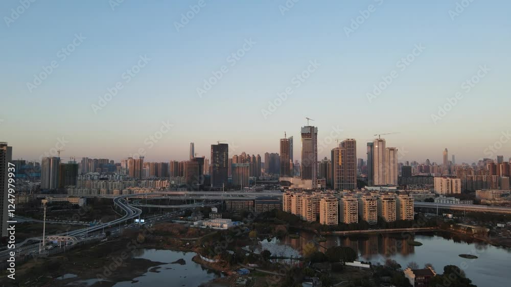Sunset view of high-rise buildings over a city with warm illumination and calm water reflection Sunset view of high-rise buildings over a city with warm illumination and calm water reflection