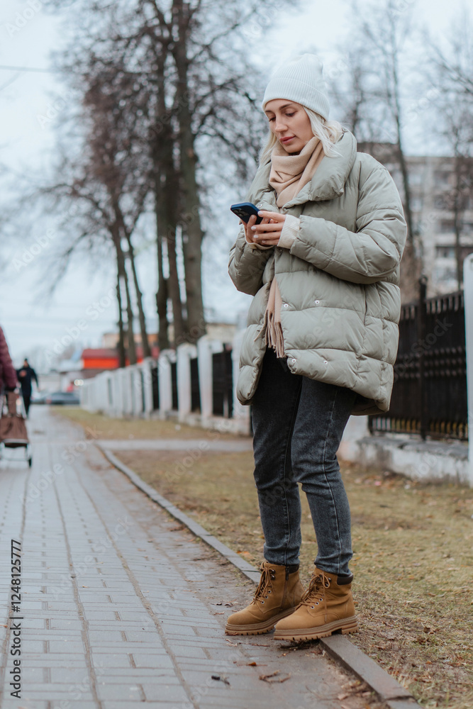 Fototapeta premium A beautiful young woman strolls through the city on a sunny autumn day, happily chatting on her phone. She smiles and laughs, radiating joy and positive energy in the vibrant urban setting