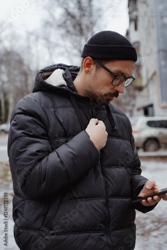 A young man in casual style walks through the snowy city on a winter day, chatting on his phone and sipping coffee. The lifestyle photo captures his relaxed, modern vibe and cheerful energy