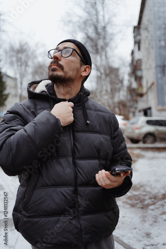 A young man in casual style walks through the snowy city on a winter day, chatting on his phone and sipping coffee. The lifestyle photo captures his relaxed, modern vibe and cheerful energy