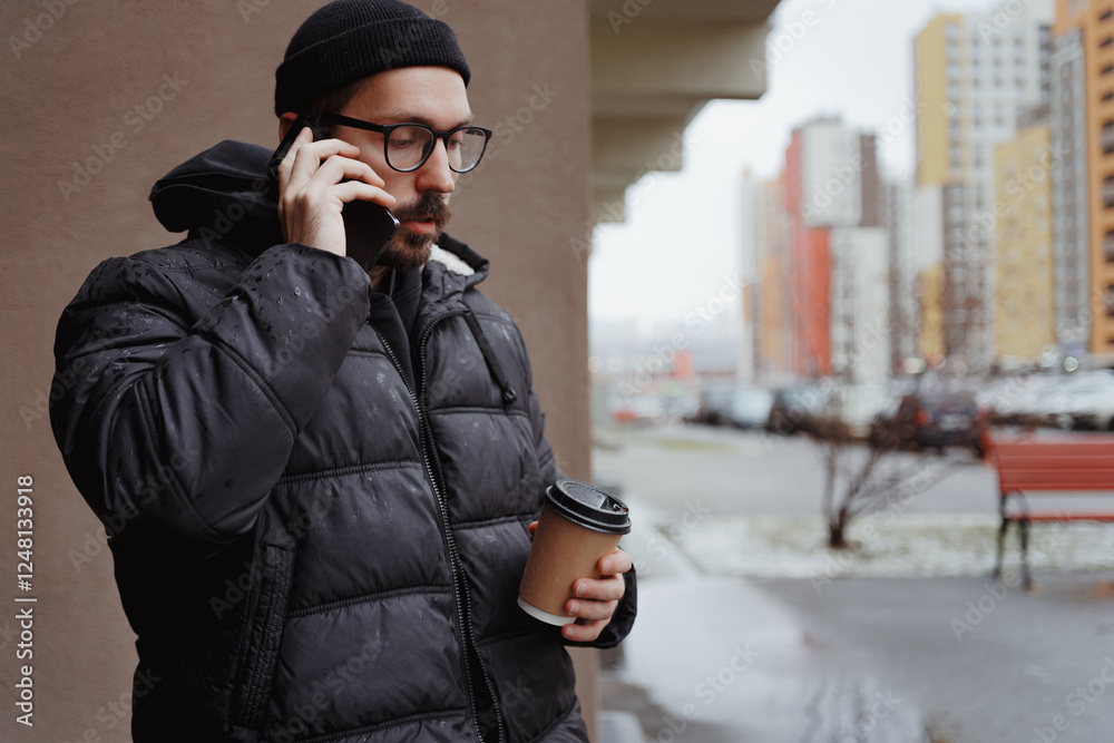 A young man in casual style walks through the snowy city on a winter day, chatting on his phone and sipping coffee. The lifestyle photo captures his relaxed, modern vibe and cheerful energy A young man in casual style walks through the snowy city on a winter day, chatting on his phone and sipping coffee. The lifestyle photo captures his relaxed, modern vibe and cheerful energy