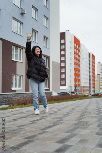 A beautiful young woman enjoys a winter day, walking through a snowy city and chatting on her phone. She laughs and smiles brightly, exuding happiness and a cozy lifestyle vibe in the urban setting