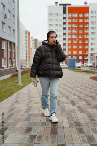 A beautiful young woman enjoys a winter day, walking through a snowy city and chatting on her phone. She laughs and smiles brightly, exuding happiness and a cozy lifestyle vibe in the urban setting