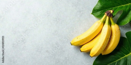 A bunch of ripe yellow bananas rests on a light gray surface, surrounded by vibrant green tropical leaves; a healthy and refreshing image.