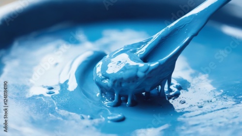 Closeup of vibrant blue paint splatter resembling a spoon, dripping on white surface with blurred background.