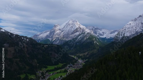 Aerial footage flying away from Piccolo Vernel, mountain in the Marmolada Range of the Dolomites in Italy with small villages underneath it. photo