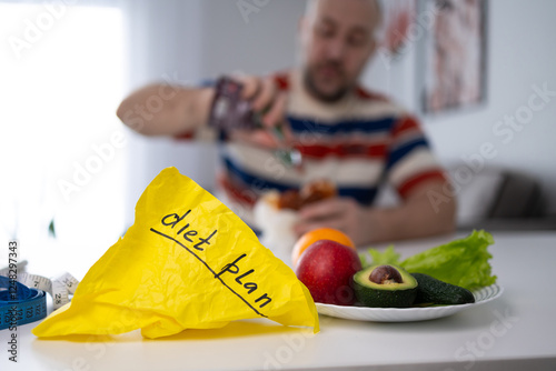 A man resolutely prepares to eat food that does not correspond to a healthy diet, neglecting the diet plan and ignoring fresh fruits and juicy vegetables.
