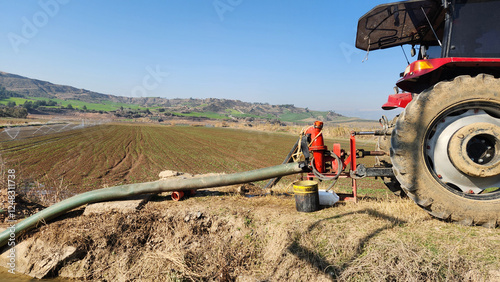 A tractor's power take-off draws water from a canal and sends it to a sprinkler system, efficiently irrigating the fields with a controlled and steady water flow.