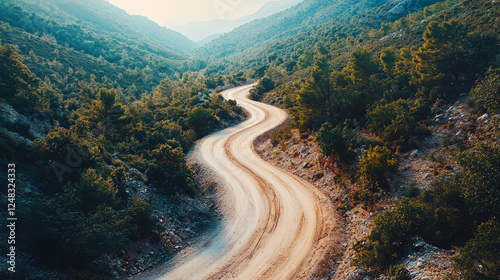 A winding dirt road cuts through lush green mountain terrain, bathed in the soft light of a misty day.
