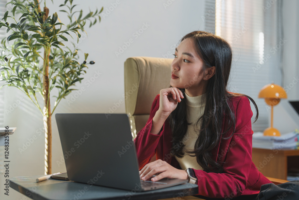 Thoughtful businesswoman in a red blazer sitting at her desk, looking away from her laptop. Modern office setting with natural light and a potted plant enhancing the workspace Thoughtful businesswoman in a red blazer sitting at her desk, looking away from her laptop. Modern office setting with natural light and a potted plant enhancing the workspace