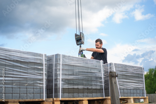 A man unloads paving stones on pallets with a truck crane