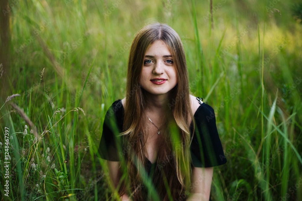 Young woman with flowing brown hair kneeling peacefully among tall green grass, wearing elegant black dress Young woman with flowing brown hair kneeling peacefully among tall green grass, wearing elegant black dress
