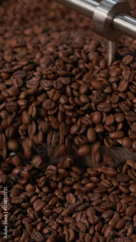 Vertical close-up shot of coffee beans being stirred in industrial roaster at coffee roasting plant