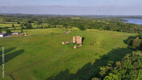 McGrath Castle, Pettigo, County Donegal, Ireland, June 2023. Drone orbits clockwise around the historic ruins surrounded by green farmland with Lower Lough Erne in the distance during golden hour. photo