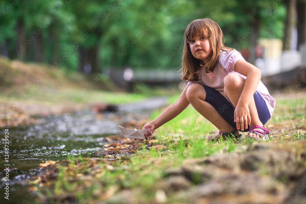 Little girl launching paper boat into stream in summer park Little girl launching paper boat into stream in summer park