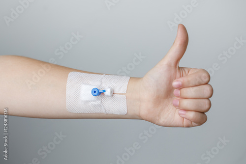 Hand with Peripheral venous catheter holding thumb up on grey background