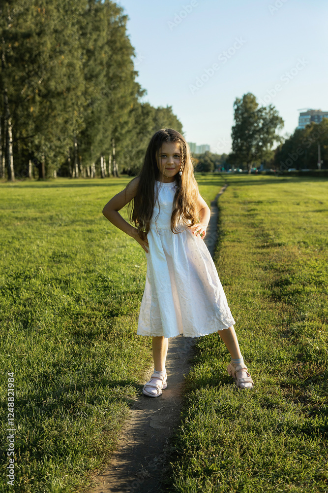 A young girl with long wavy brown hair stands in a sun-drenched green field in a white dress. Sunlight illuminates her hair. A young girl with long wavy brown hair stands in a sun-drenched green field in a white dress. Sunlight illuminates her hair.