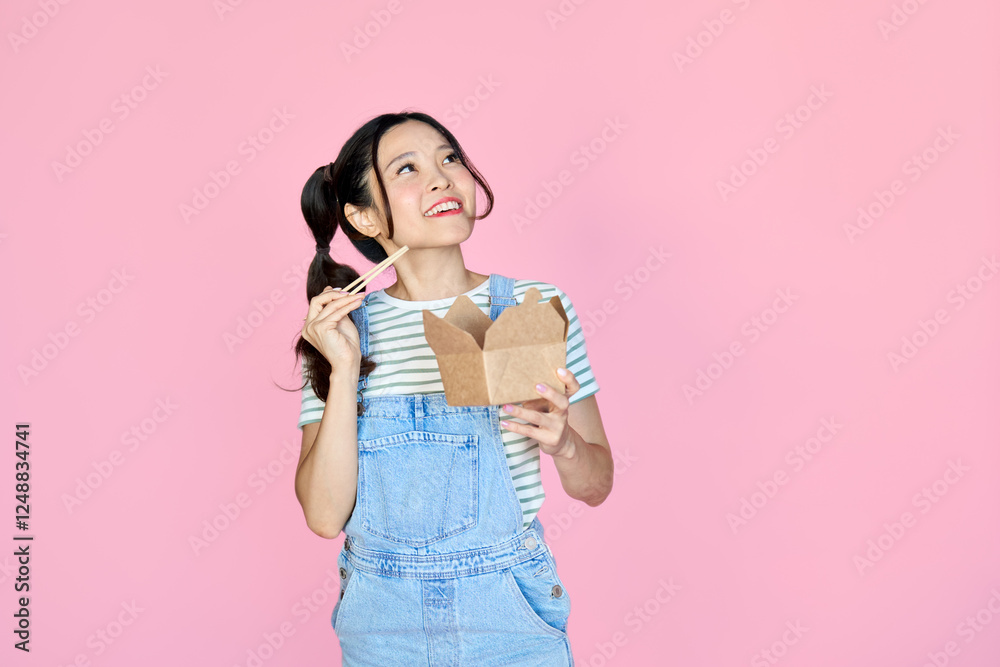 Happy young Asian woman customer having fun holding chopsticks and Asia food delivery box ordering sushi or noodles takeout in takeaway restaurant looking at copy space isolated on pink background. Happy young Asian woman customer having fun holding chopsticks and Asia food delivery box ordering sushi or noodles takeout in takeaway restaurant looking at copy space isolated on pink background.