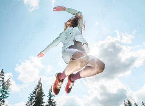 Low angle female athlete jumping against scenic view of blue sky