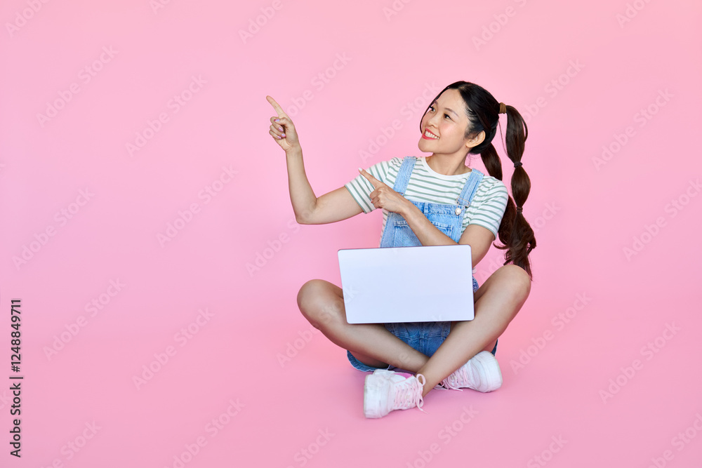 Happy pretty young Asian woman with laptop, smiling student girl with ponytails holding computer pointing aside presenting elearning online, websites, web services sitting isolated on pink background. Happy pretty young Asian woman with laptop, smiling student girl with ponytails holding computer pointing aside presenting elearning online, websites, web services sitting isolated on pink background.
