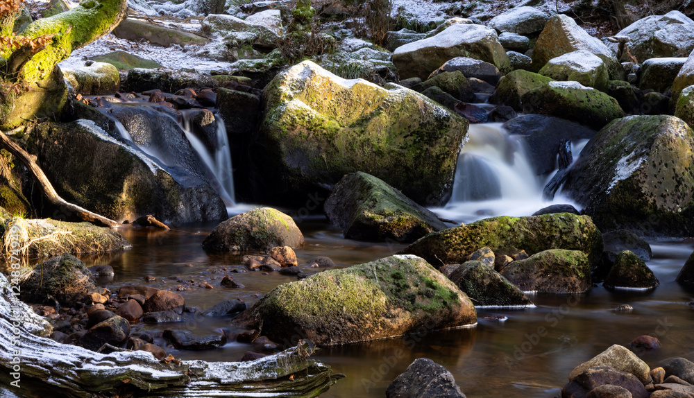 Naklejka premium Long Exposure image of a stream tumbling between moss-covered rocks with a dusting of snow