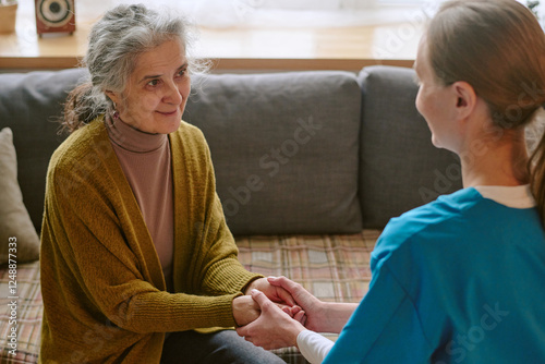 High angle shot of senior woman looking at nurse with smile while she holding her hands