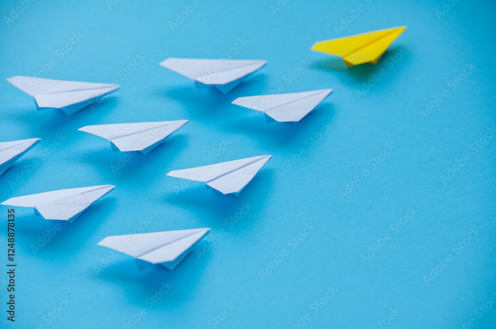 Close up view of yellow paper airplane origami leading white airplanes on blue background with customizable space for text. Business and Leadership skills concept Close up view of yellow paper airplane origami leading white airplanes on blue background with customizable space for text. Business and Leadership skills concept