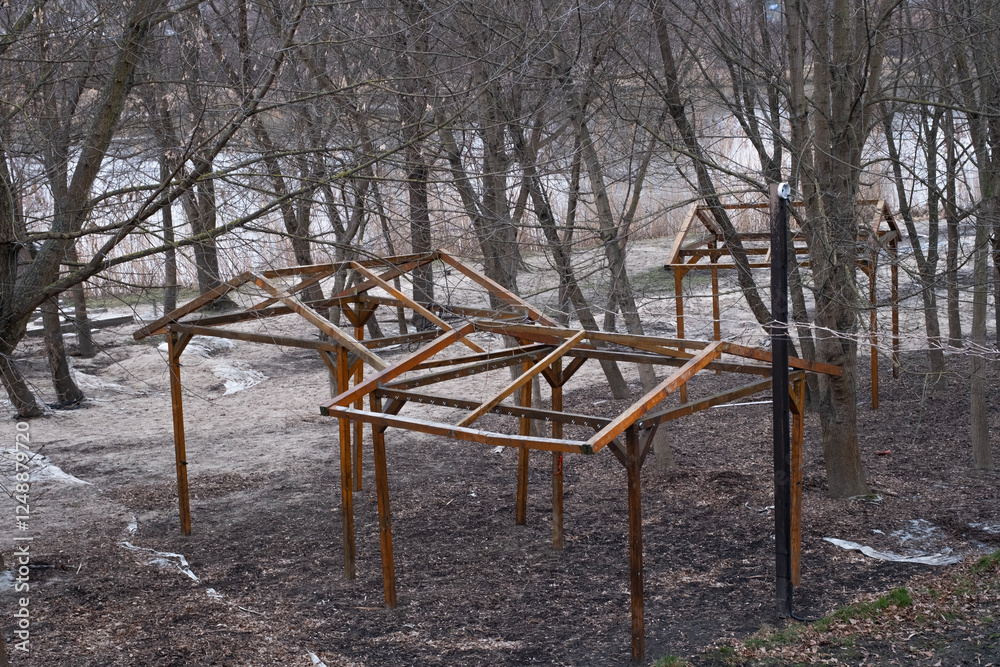 Fototapeta premium Several unfinished wooden gazebo frames in a natural setting, likely part of an ongoing park development or outdoor shelter project. 