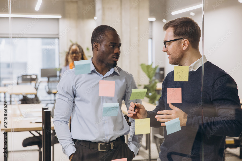 Two business professionals discussing ideas in a contemporary office environment, surrounded by colorful sticky notes on a glass wall Two business professionals discussing ideas in a contemporary office environment, surrounded by colorful sticky notes on a glass wall