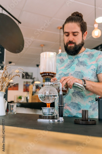 Barista expertly adding specialty coffee into a Japanese siphon coffee maker in modern cafe setting, focusing on the art of beverage preparation. The process involves precision and attention to detail