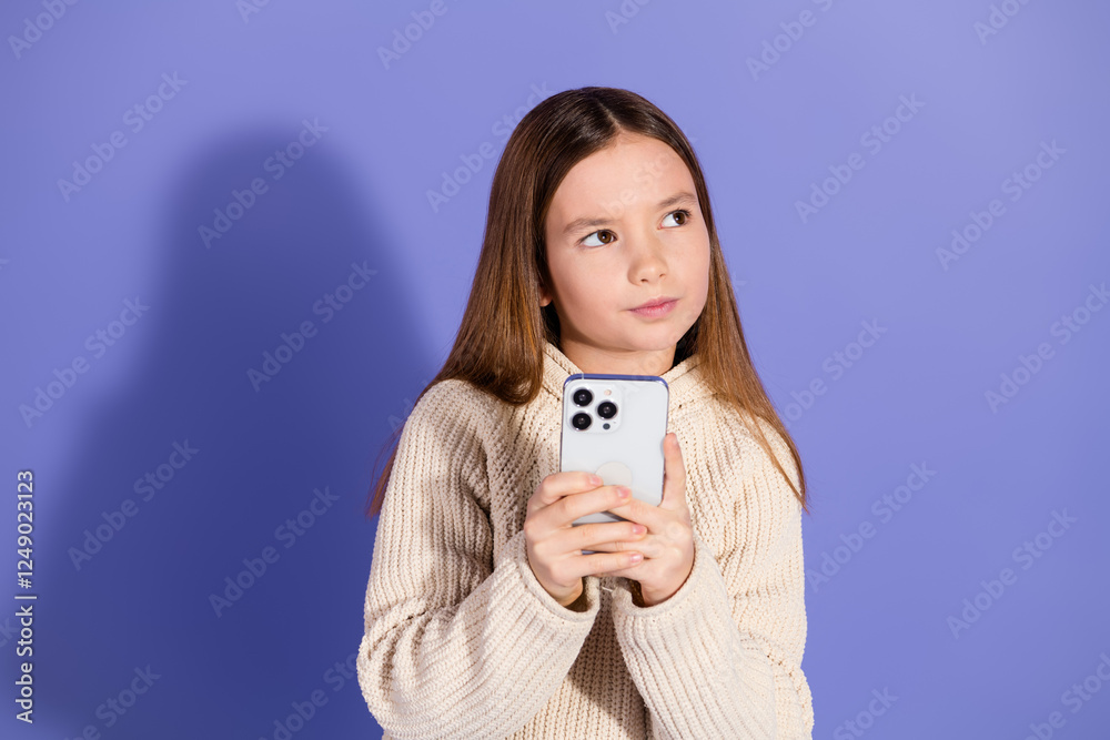 Young girl holding a smartphone against a purple background, displaying casual style and thoughtful expression. Young girl holding a smartphone against a purple background, displaying casual style and thoughtful expression.
