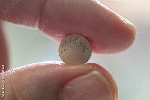 Fingers holding losartan drug tablet high blood pressure medicine - close-up	 photo