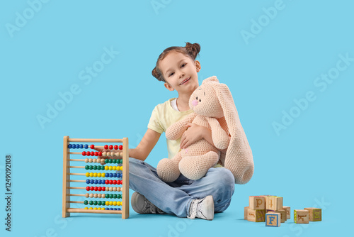 Cute little girl with toy bunny and abacus sitting on blue background