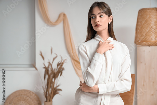 Pretty young woman in stylish outfit among decor near white wall