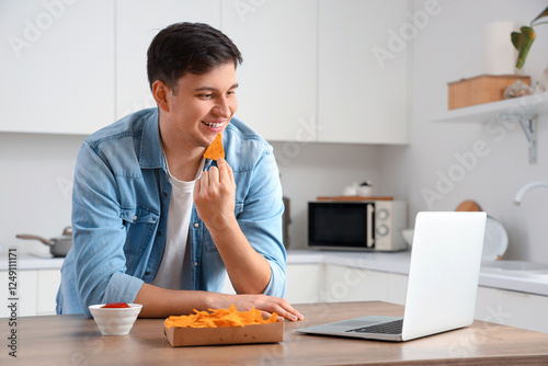 Young man with laptop eatin...